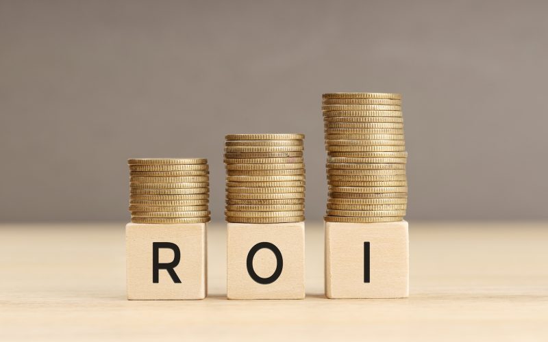 ROI word in wooden blocks with coins stacked in increasing stacks. Return on investment concept. Copy space